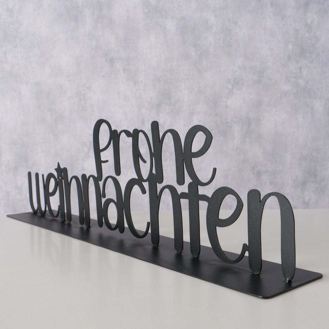 Schwarzer metallener Schriftzug „Frohe Weihnachten“ als dekorativer Aufsteller im modernen, matten Design